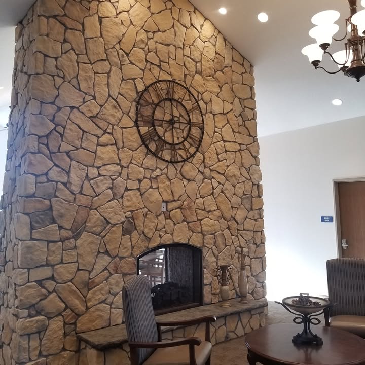 Completed floor-to-ceiling stone fireplace with a clock above the hearth in a furnished sitting area
